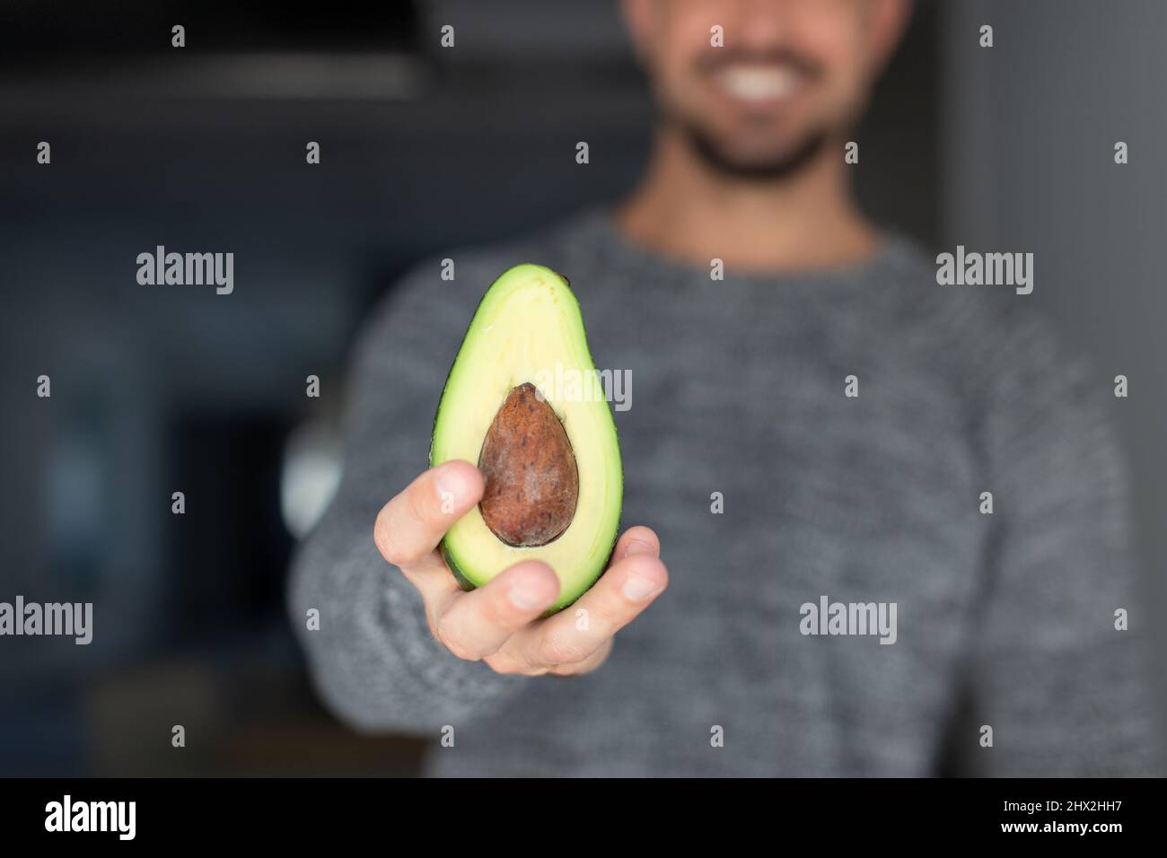 Young Caucasian 30s man holding halved acovado, toothy smile, depth of field Stock Photo