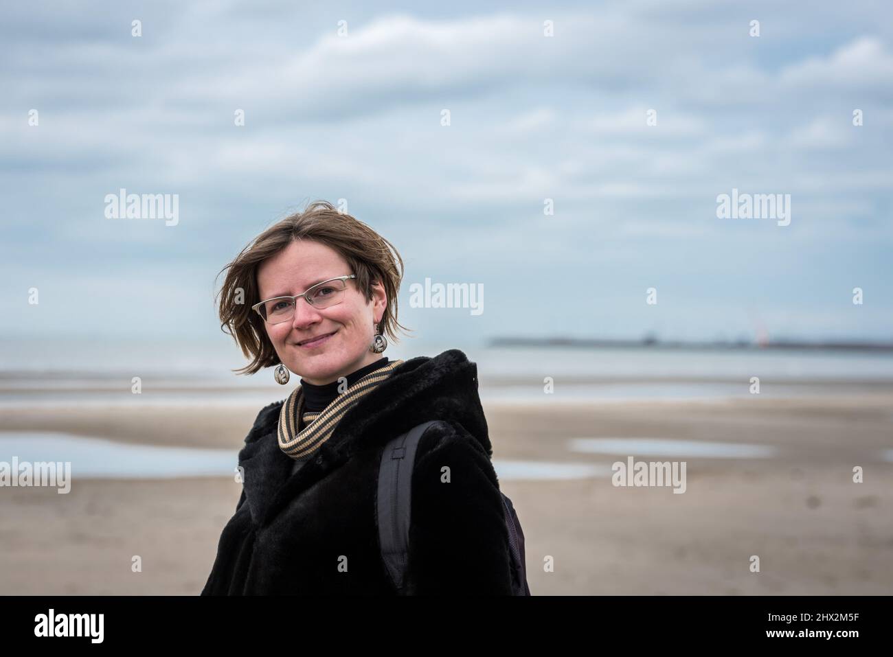 Portrait of a 30 year old white woman, standing on the beach with winter clothes. Stock Photo