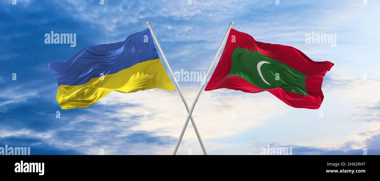 two crossed flags Maldives and Ukraine waving in wind at cloudy sky ...