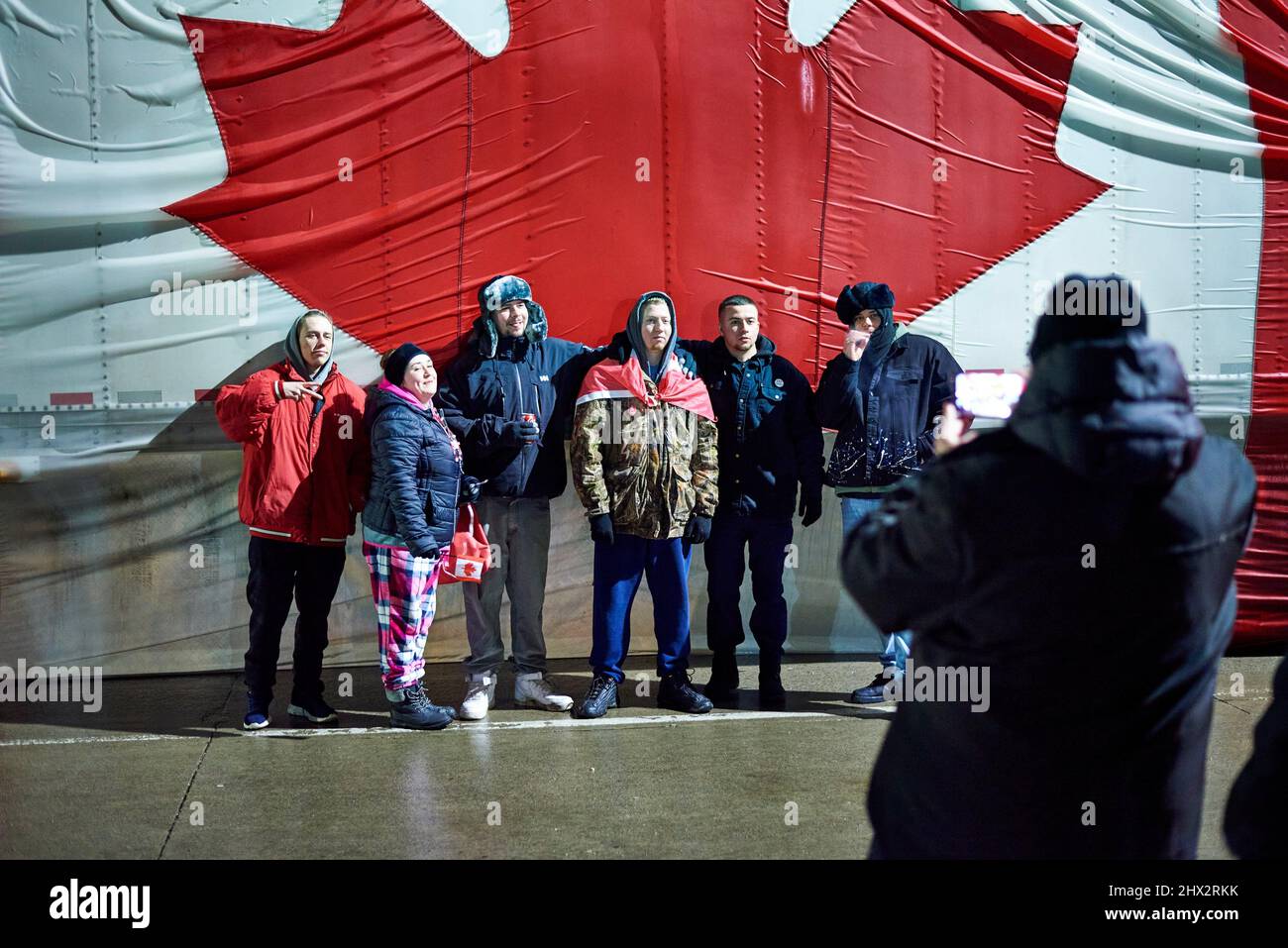 A group of six people pose in front of a large Canadian flag on the side of a semi-trailer truck on 11 February 2022 in Windsor, Ontario on day five Stock Photo