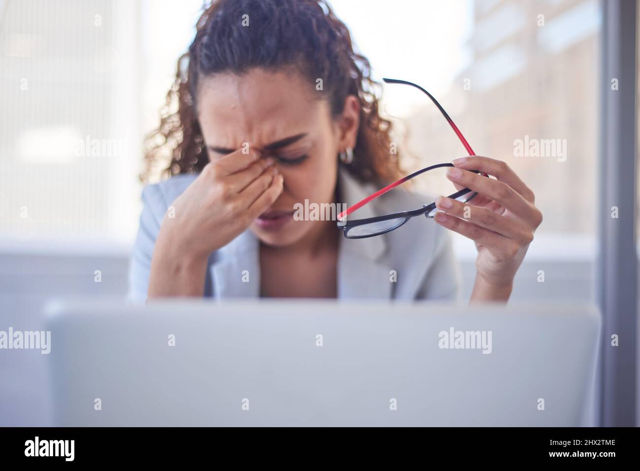 Selective focus on eyeglasses as a woman rubs her eyes due to eye strain Stock Photo