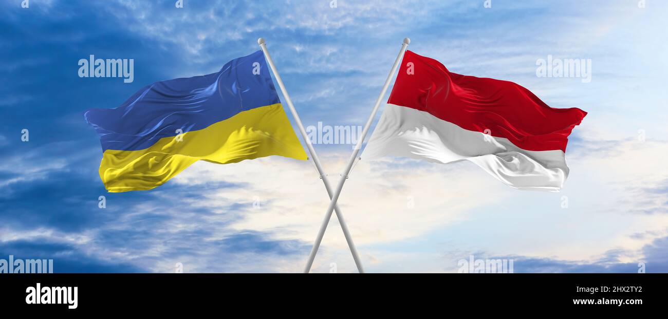 two crossed flags Monaco and Ukraine waving in wind at cloudy sky ...