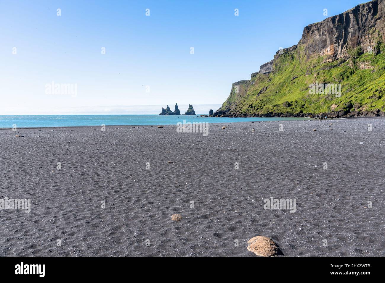 View of a black sand beach with people horseback riding on a clear