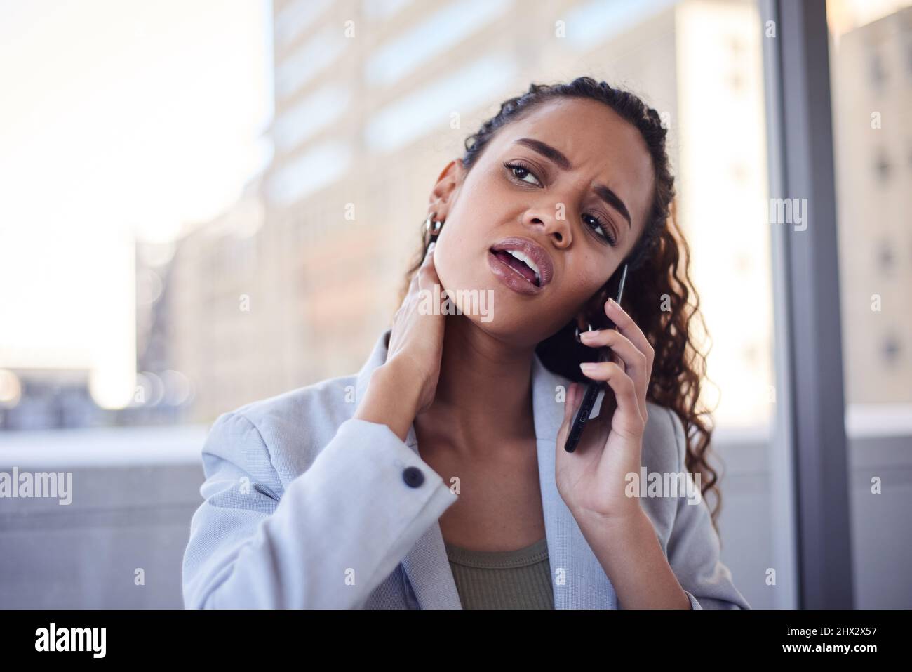 A young business woman rubs her neck while on a call in the city office ...
