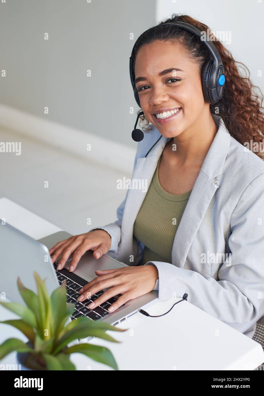 A young call centre agent looks up smiling from her desk while typing Stock Photo
