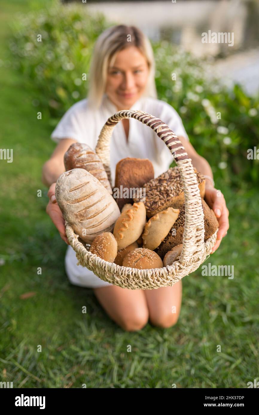 Young woman in white dress sitting on the grass with basket with assorti of brown and white homemade bread. High quality photo Stock Photo