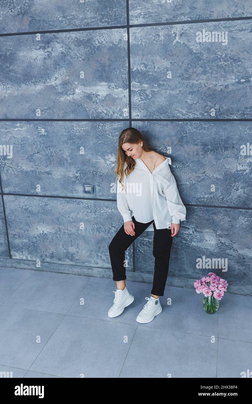 Playful self-confident woman in a stylish cotton white shirt, black jeans,  white leather sneakers, casual style.Blond-haired woman on a gray backgroun  Stock Photo - Alamy