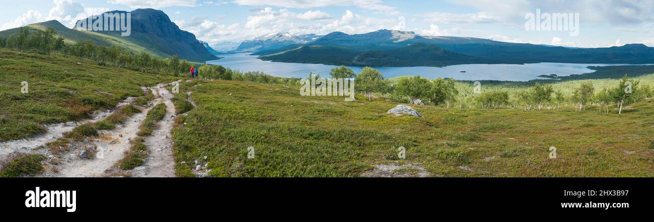 Panoramic landscape with beautiful river Lulealven, snow capped mountain, birch trees and two hikers couple at Kungsleden hiking trail near Stock Photo