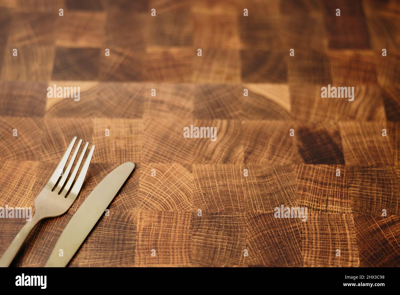 A dining gold fork and knife sitting on top of an empty butcher block counter top in a kitchen Stock Photo