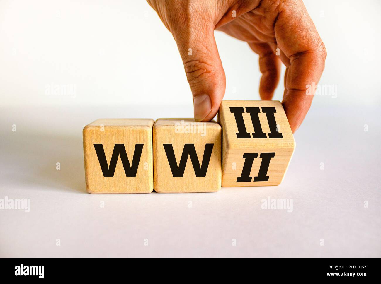 WW3 world war 3 symbol. Businessman turns the wooden cube and changes the concept word WW2 to WW3. Beautiful white table white background, copy space. Stock Photo