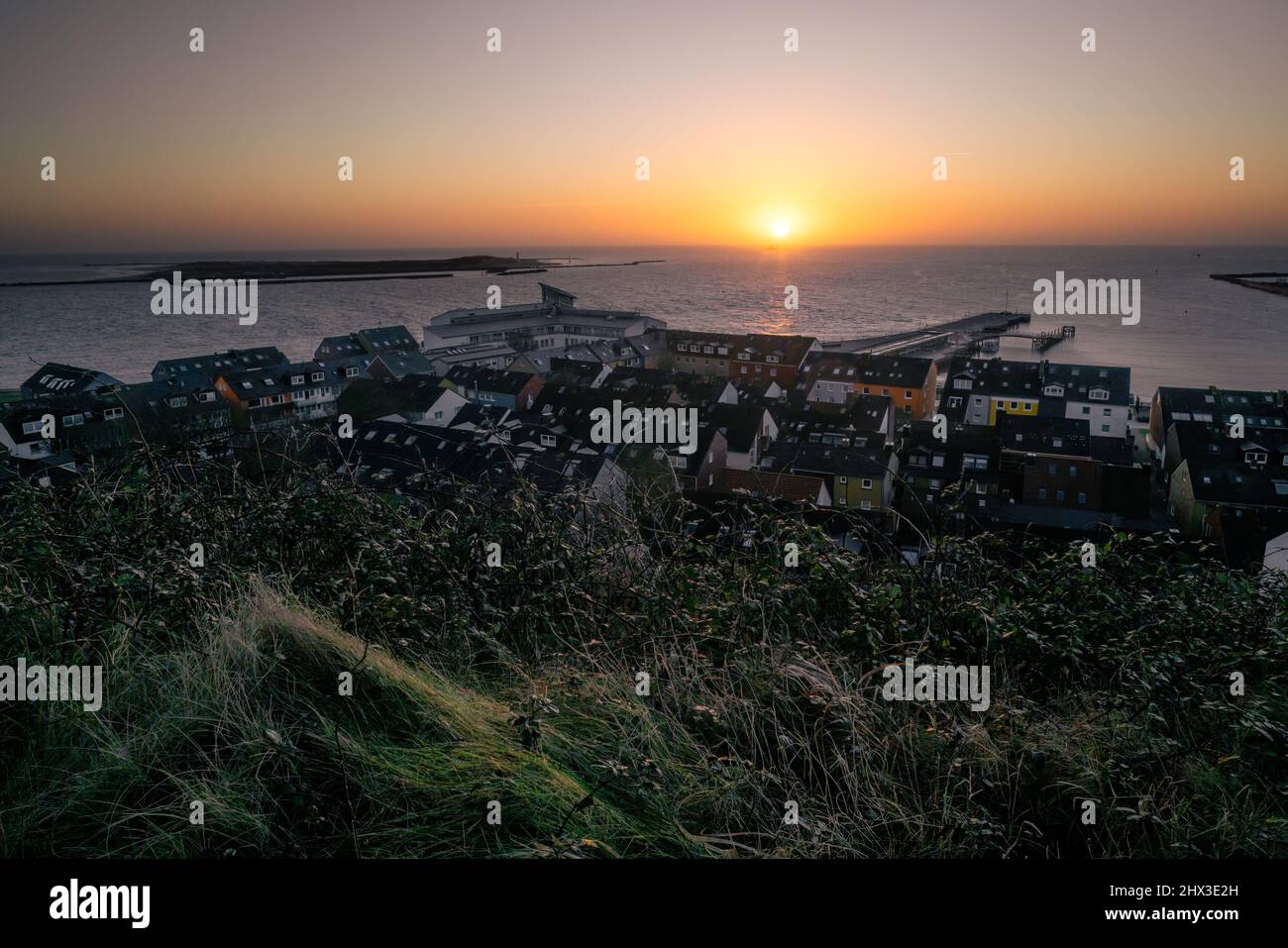 Sunrise above small port city of Helgoland, Germany. Sunrise colors in the sky. Sun disc rising on the distant horizon. Stair leading down to the city Stock Photo