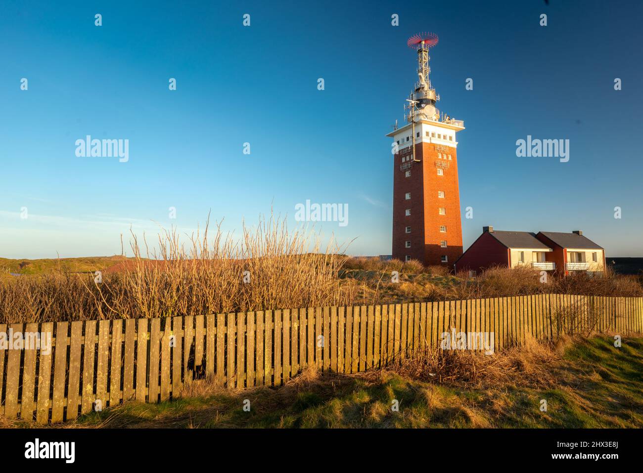 Golden hour by the lighthouse on the Heligoland, or Helgoland island, Germany. Clear blue sky and old wooden fence in the front. Exploring German Stock Photo