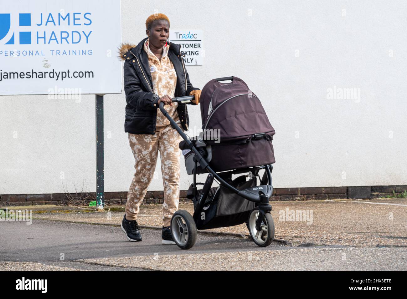 Young black or African woman mother walking down the street pushing her baby in a pram, UK Stock Photo