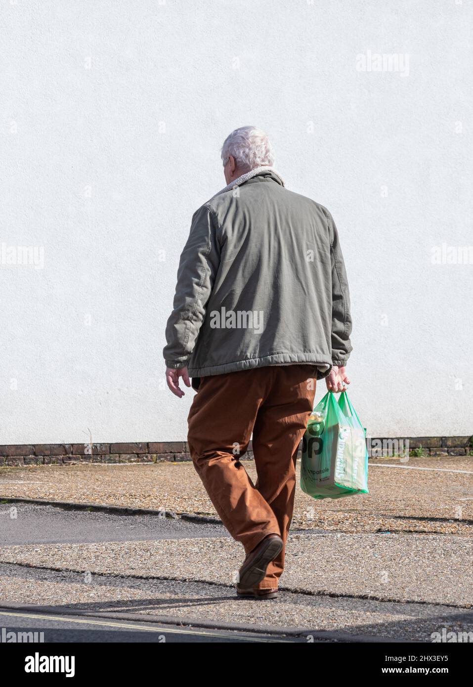 Senior man walking back from the shop or store carrying a plastic Co-op supermarket carrier bag, UK Stock Photo