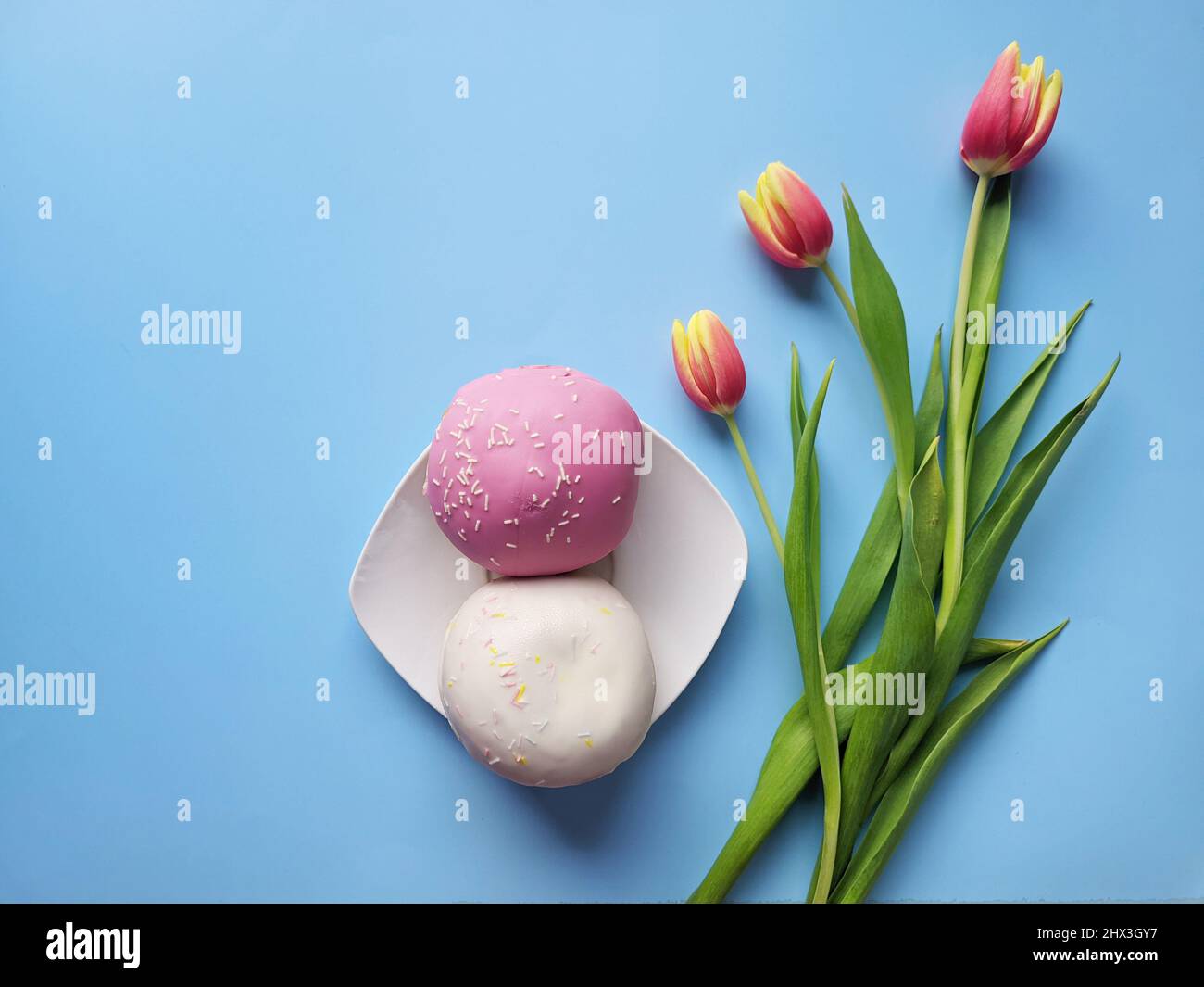 Morning with cup of hot coffee and sweet donuts on blue background. Bouquet of tulips. Top view, copy space, mockup. Flat lay. Food and drinks. Spring Stock Photo