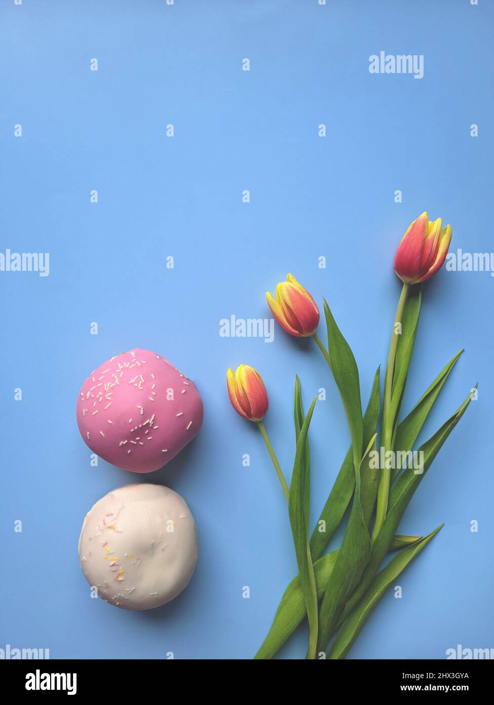 Morning with cup of hot coffee and sweet donuts on blue background. Bouquet of tulips. Top view, copy space, mockup. Flat lay. Food and drinks. Spring Stock Photo
