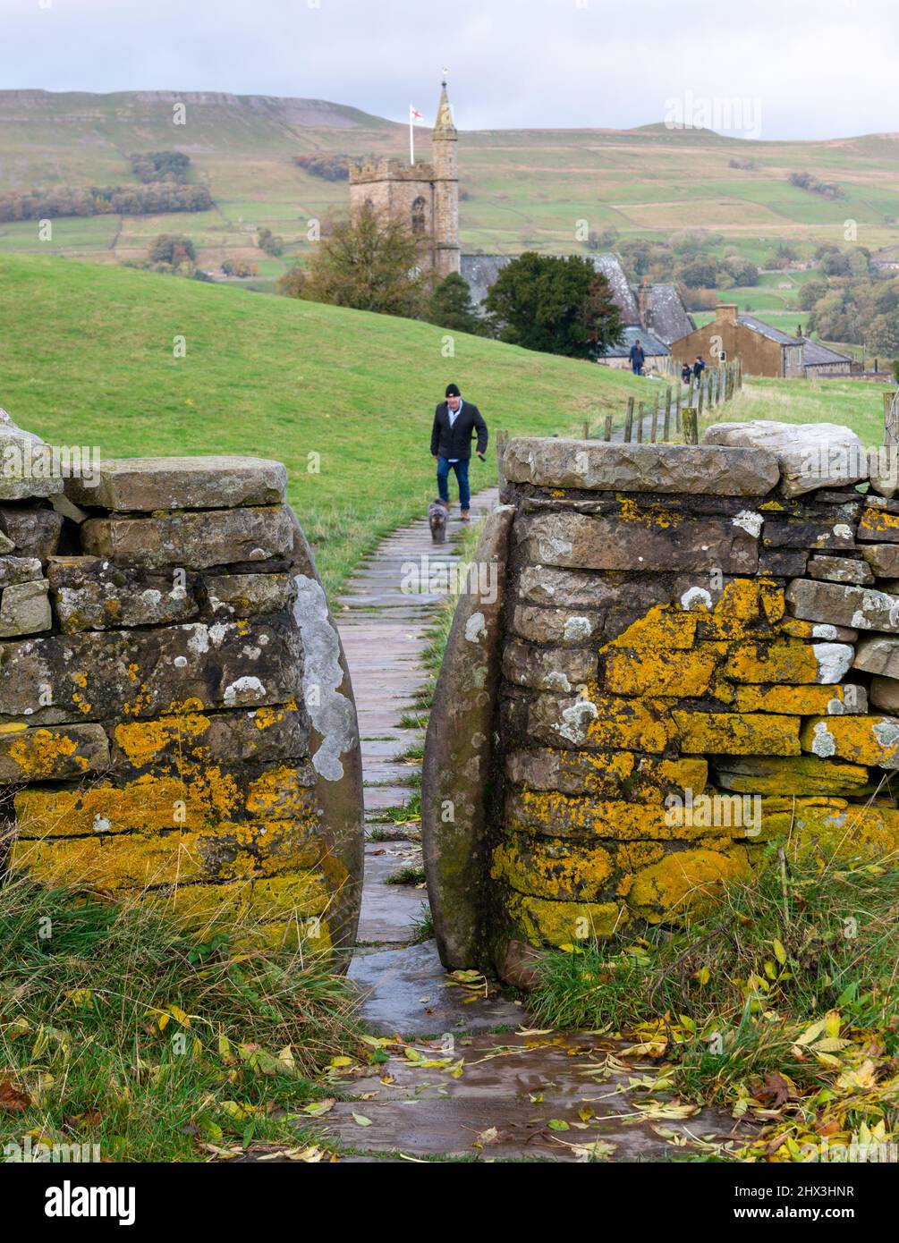 A man walking his small dog towards a squeeze stile on a footpath at Bealer Bank, in Hawes, Wensleydale Stock Photo