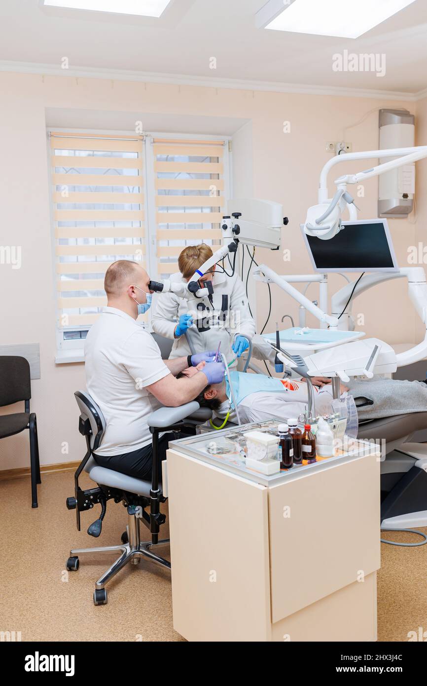 The dentist is in his dental office. A dentist in a white uniform treats a patient's teeth with