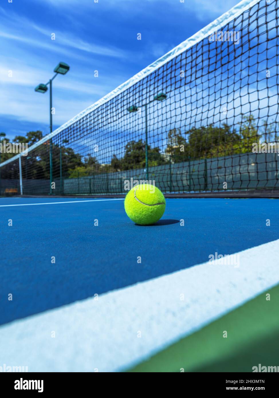 Yellow tennis ball on blue court with black net. Stock Photo