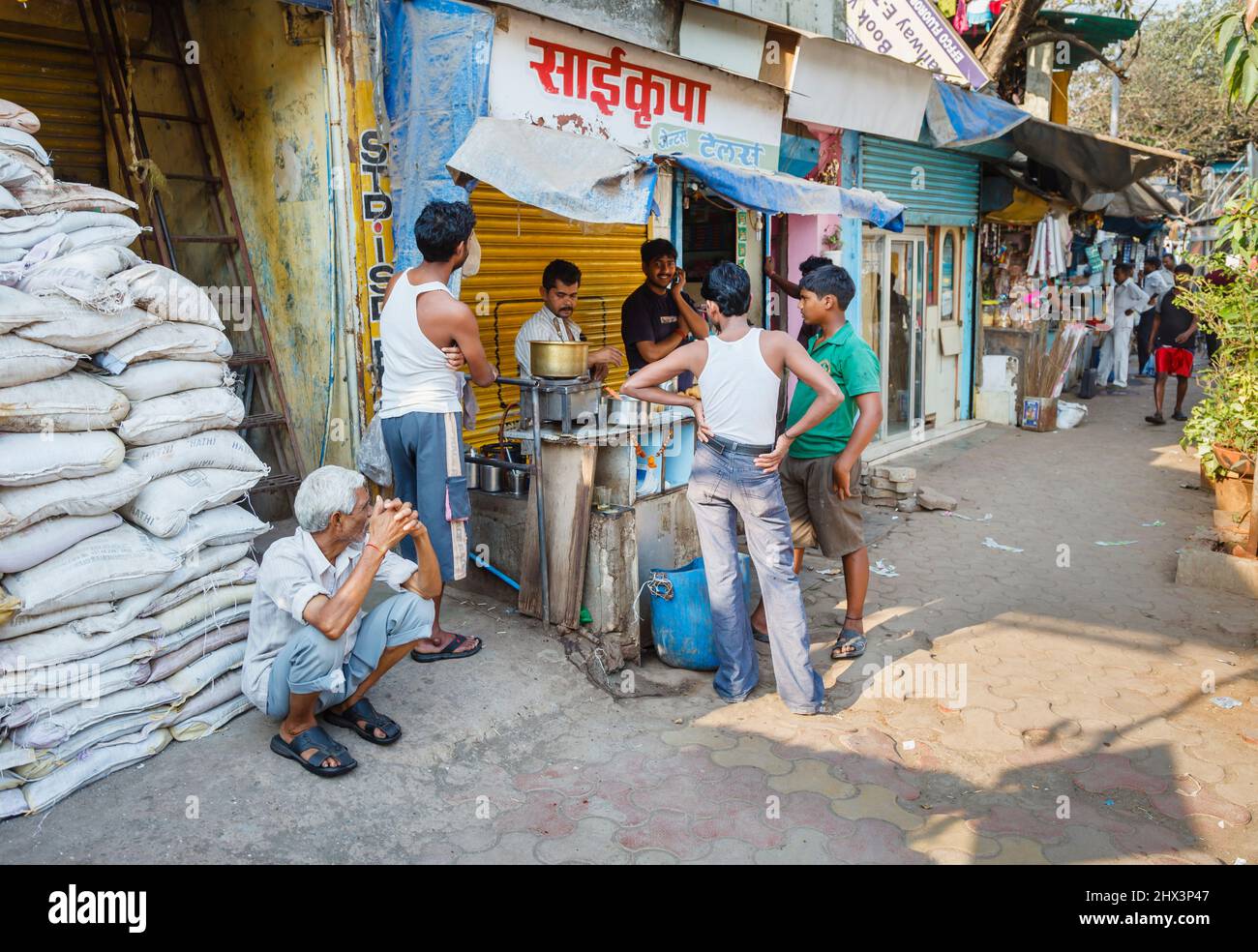Local men gather round a street food seller and a man squats beside food sacks outside Mahalaxmi Dhobi Ghat, a large open air laundry in Mumbai, India Stock Photo