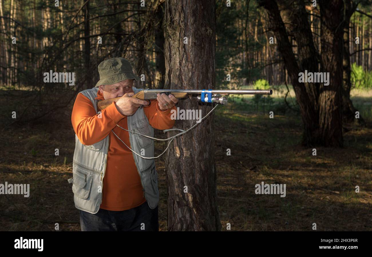 Ukrainian senior aim rifle in dark forest leaning on a pine tree Stock Photo