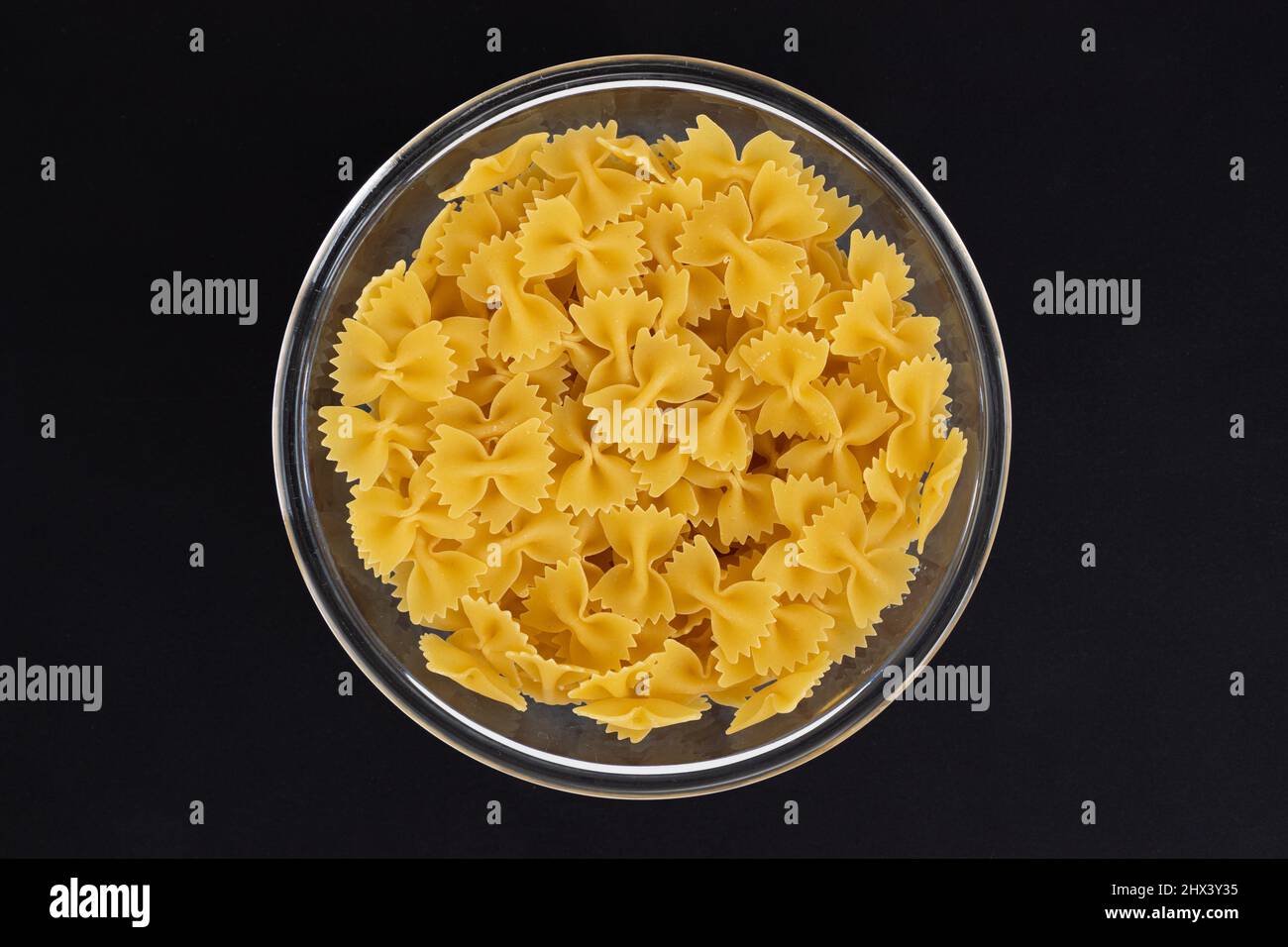 pasta farfalle in glass bowl isolated on black background, raw pasta in shape of bow, top view Stock Photo