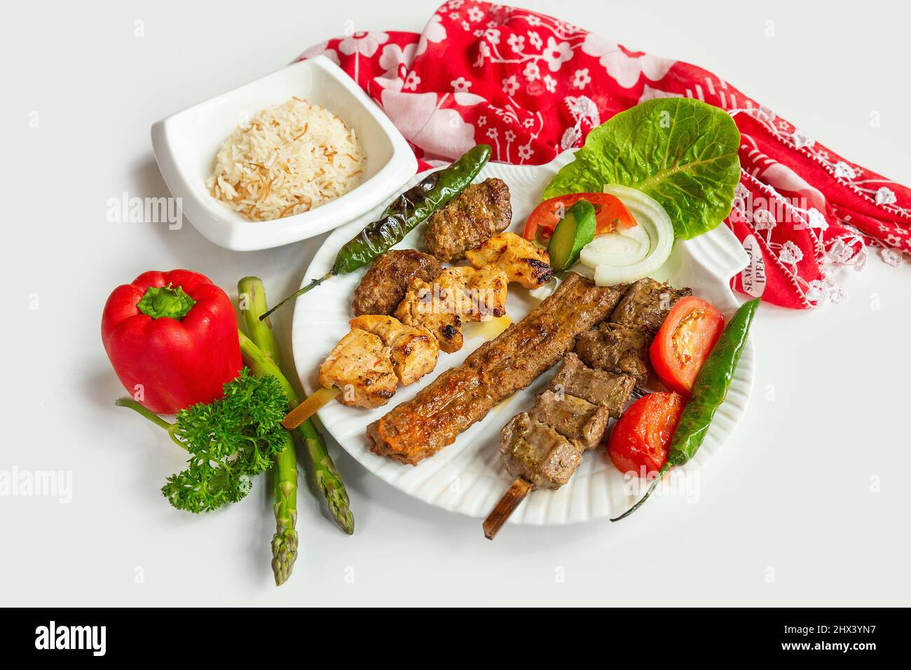 Selection of BBQ chicken tikka and seekh kebabs served with rice salad in a dish isolated on colorful table cloth top view on grey background Stock Photo