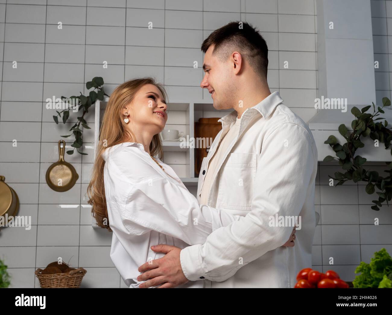Loving couple hugging in kitchen while cooking. Handsome man and beautiful woman looking at each other with smile. High quality photo Stock Photo