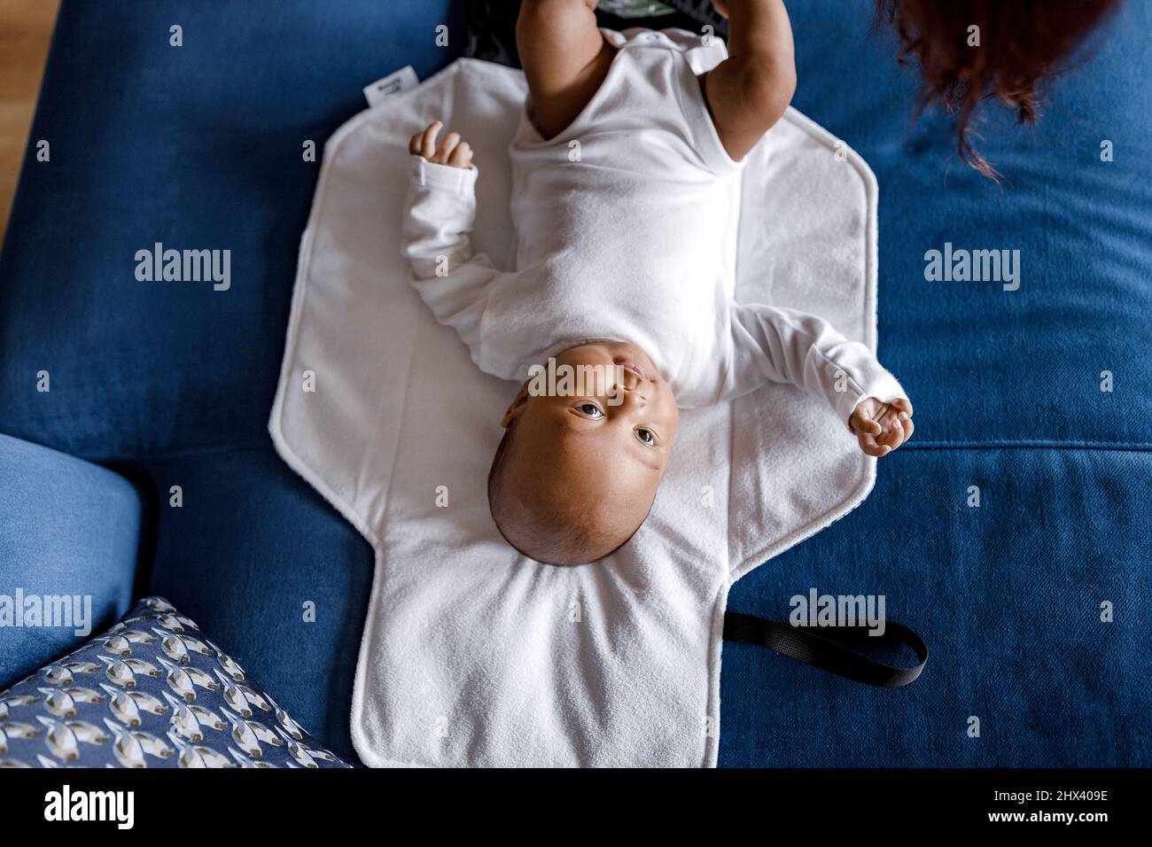 Top view of newborn Afro American baby boy looking at camera and laying with blanket on sofa, while mother changes clothes and diapers. African Americ Stock Photo
