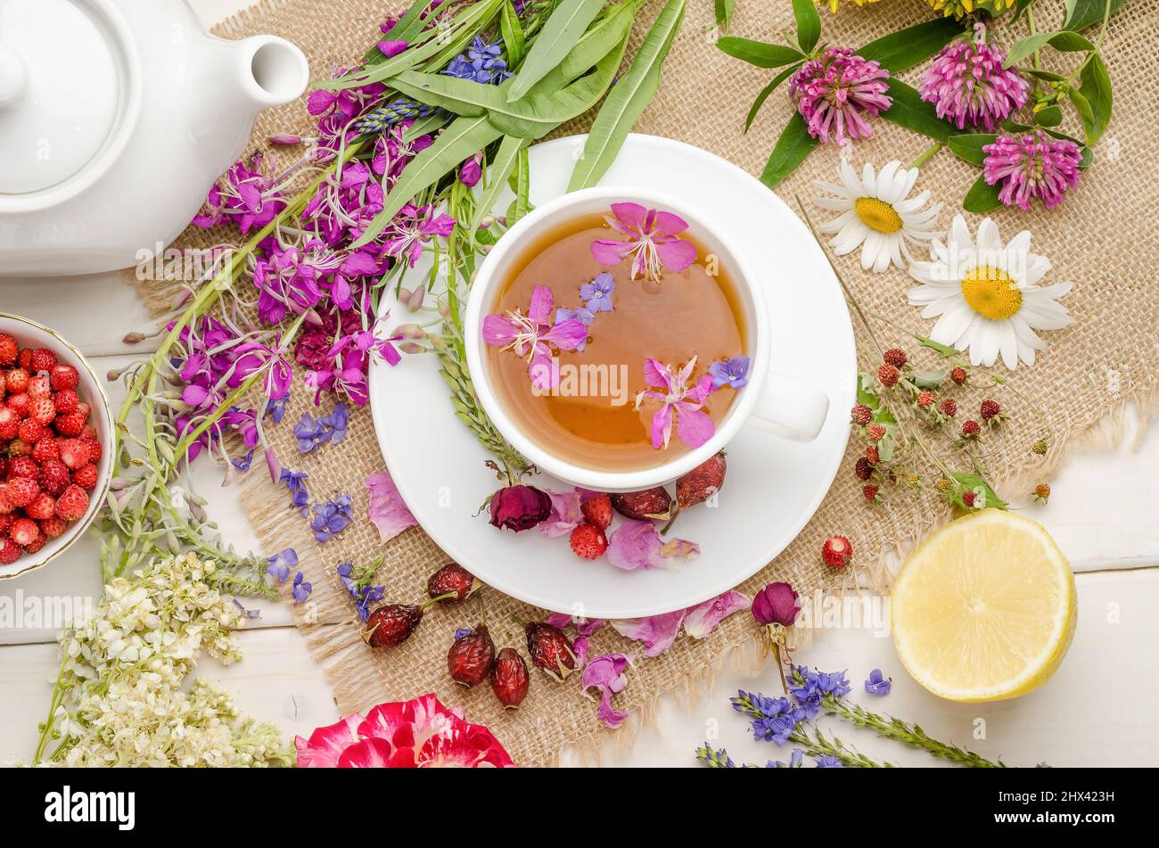 Herbal tea with rosehip, chamomile and lemon in a white cup on a white wooden table with flowers, flat lay Stock Photo