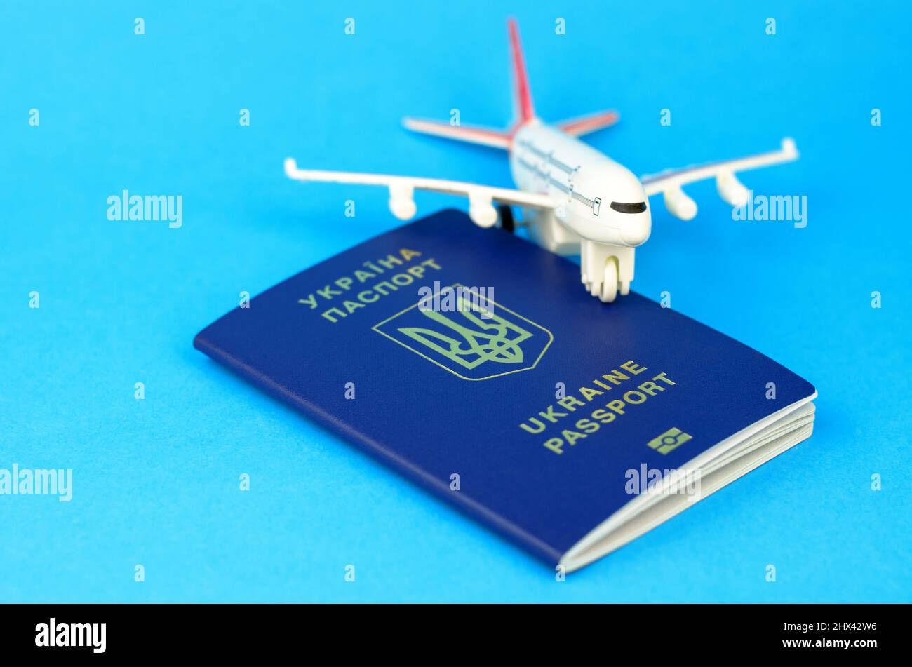 Ukrainian passport and a toy plastic plane on a blue background. Departure of Ukrainians abroad Stock Photo