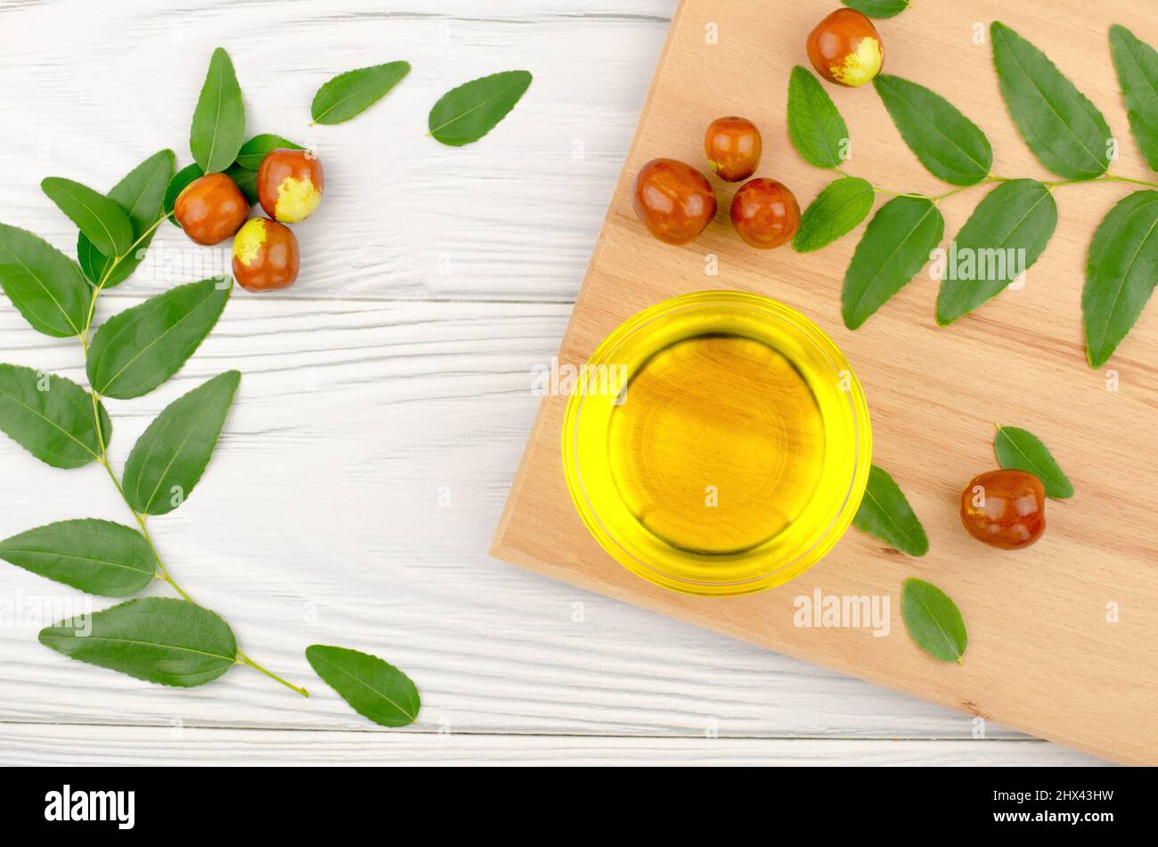 Jojoba oil in a bowl, a sprig of jojoba and fruits on a wooden table, top view Stock Photo