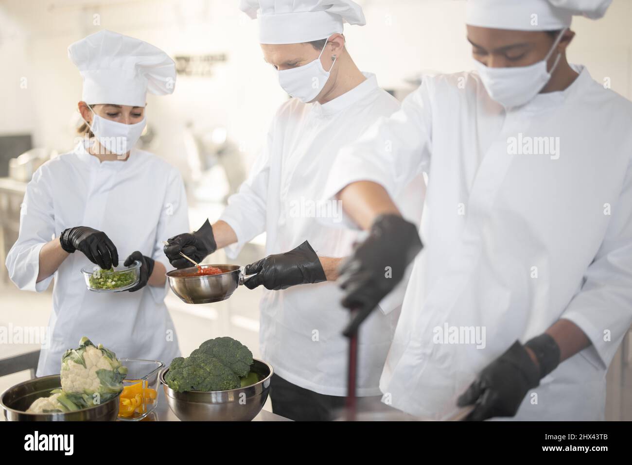 Multiracial team of chef cooks in white uniform cooking together in the