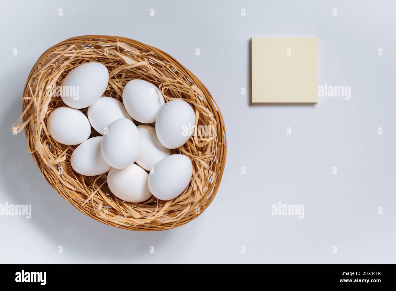 White easter eggs in yellow basket with straw on white background. Top view of Happy Easter postcard concept Stock Photo