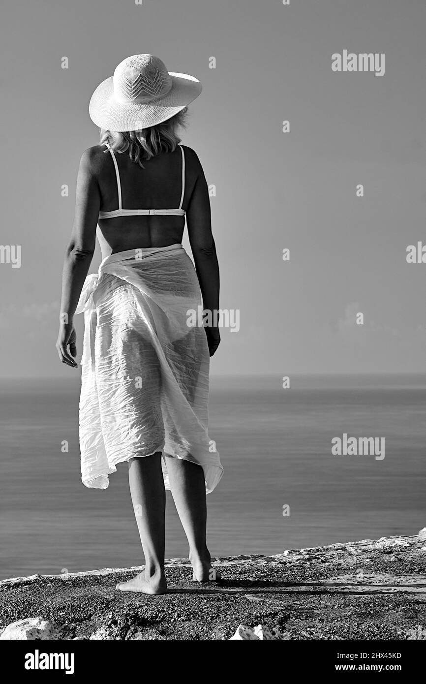 Girl in white bikini and hat on a rock by the sea in Greece, monochrome Stock Photo