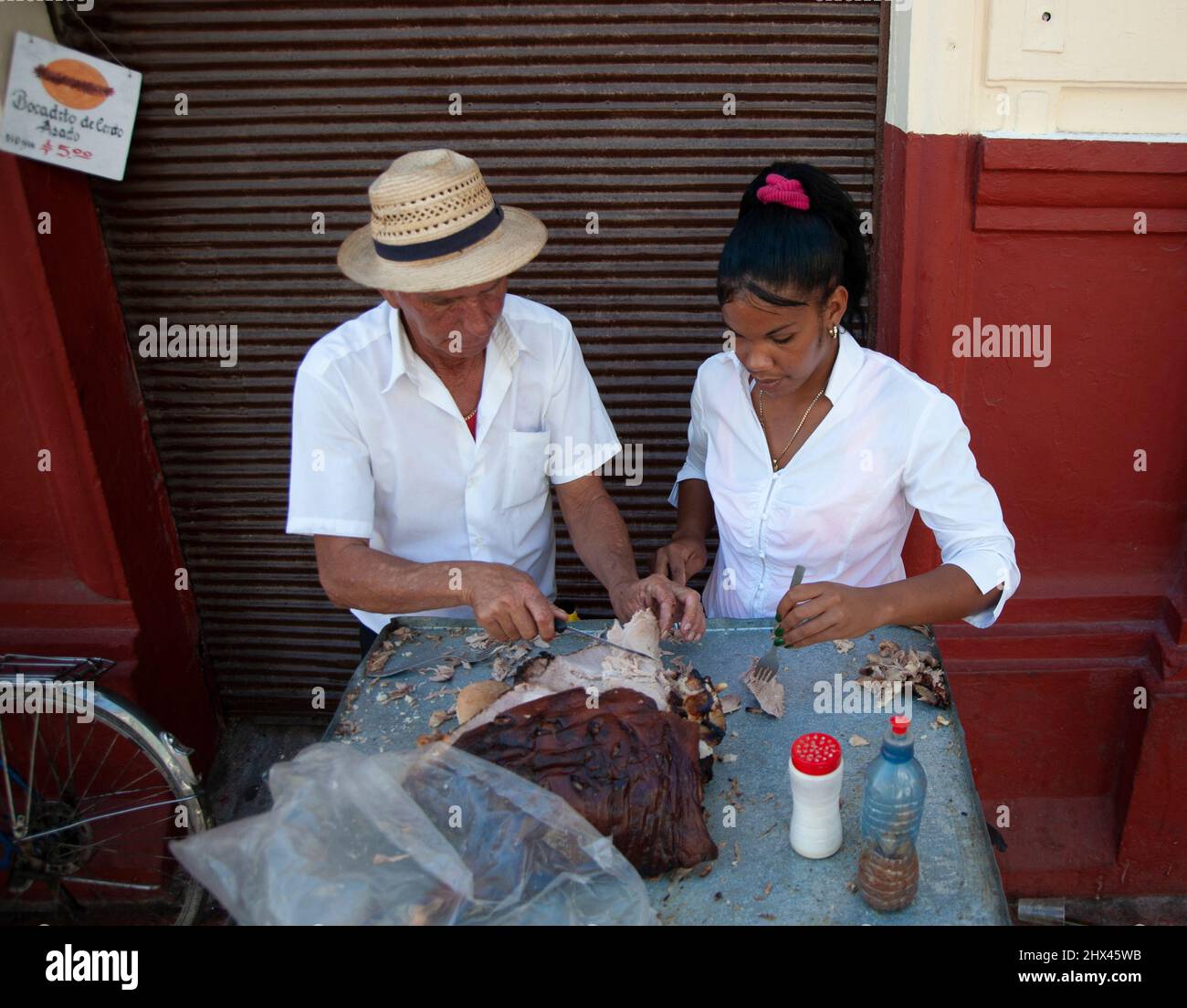 Chef wearing a fedora hat, prepares food with a waitress at an eatery in Havana, Cuba Stock Photo