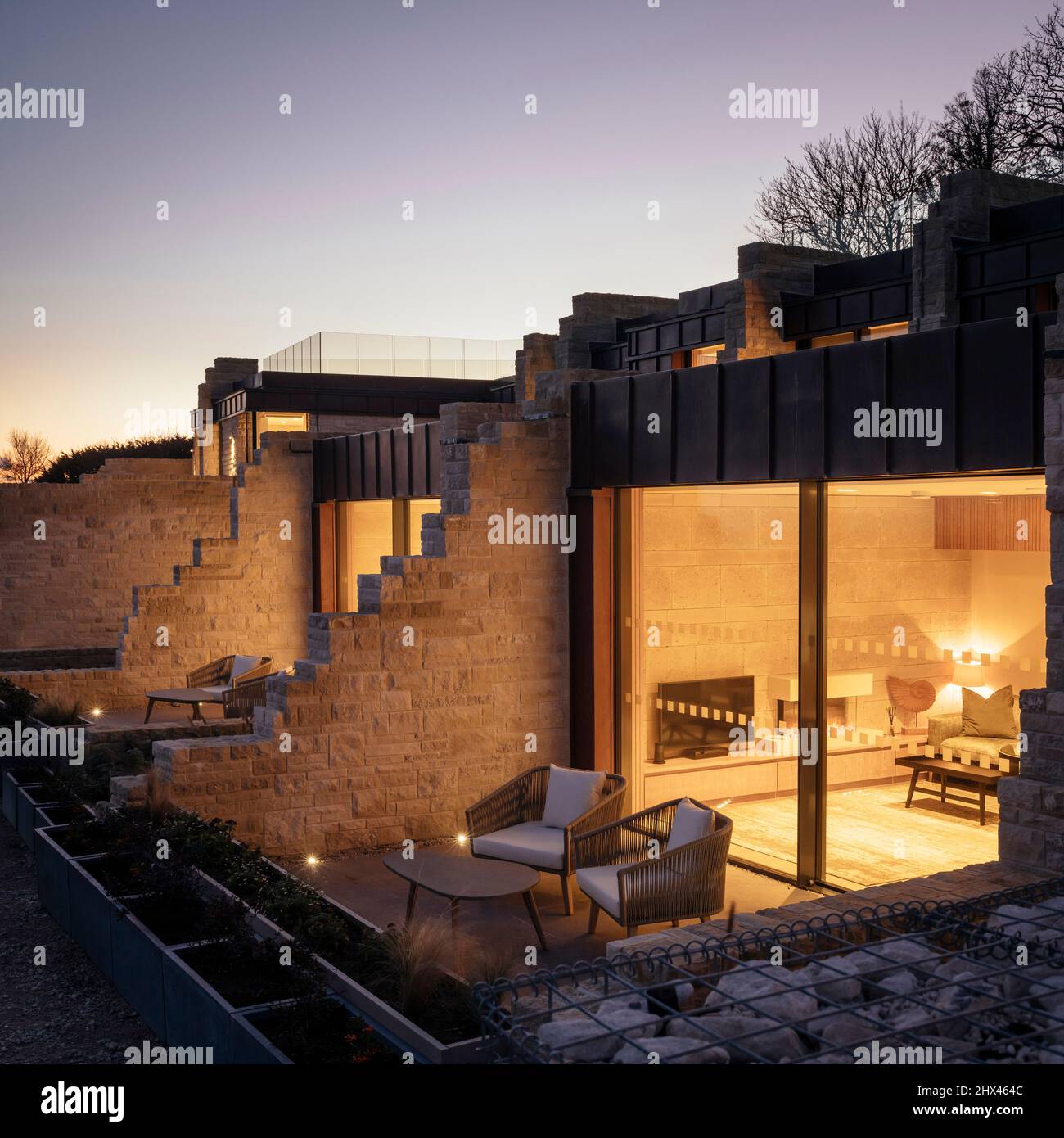 Dusk exterior view of illuminated windows and private seating area and