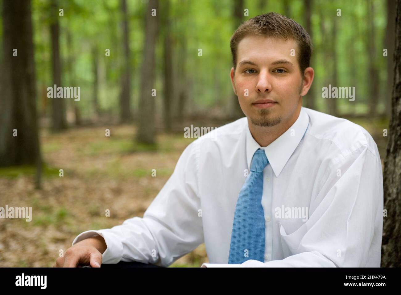 PORTRAIT OF SERIOUS YOUNG BUSINESSMAN SITTING IN TEMPERATE MIXED NORTHERN FOREST Stock Photo