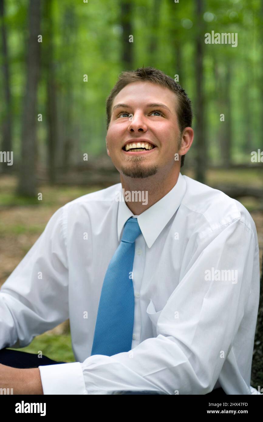 PORTRAIT OF SMILING YOUNG BUSINESSMAN SITTING IN MIXED  NORTHERN FOREST Stock Photo