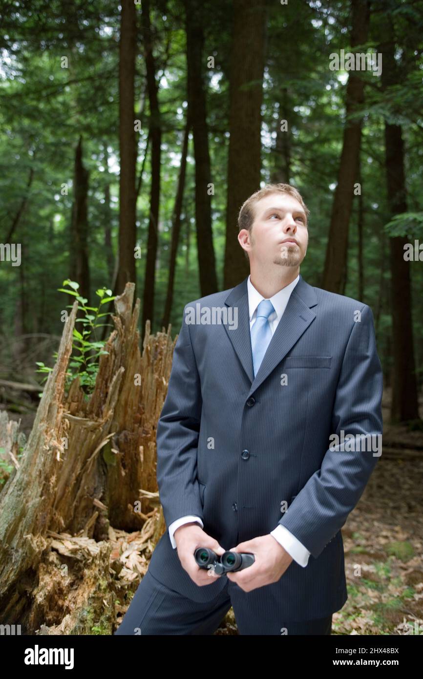 YOUNG BUSINESSMAN HOLDING BINOCULARS IN TEMPERATE MIXED NORTHERN FOREST Stock Photo
