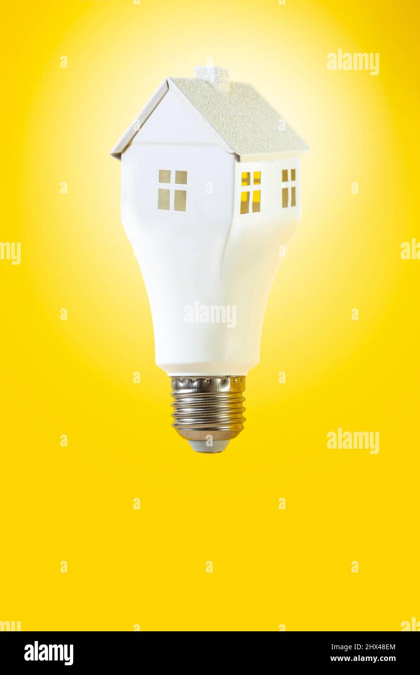 Levitating lightbulb in the form of a white house, isolated on yellow background. Home shape light bulb Stock Photo