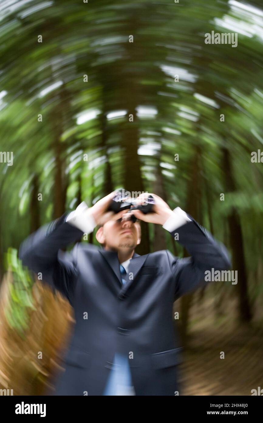 SPINNING EFFECT YOUNG BUSINESSMAN LOOKING THROUGH BINOCULARS IN TEMPERATE MIXED NORTHERN FOREST Stock Photo