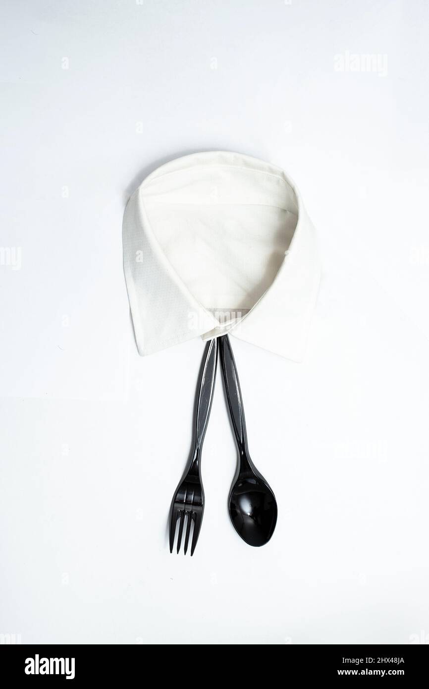 Black plastic fork and spoon, used as a tie on a white shirt collar. Restaurant wall art photography Stock Photo