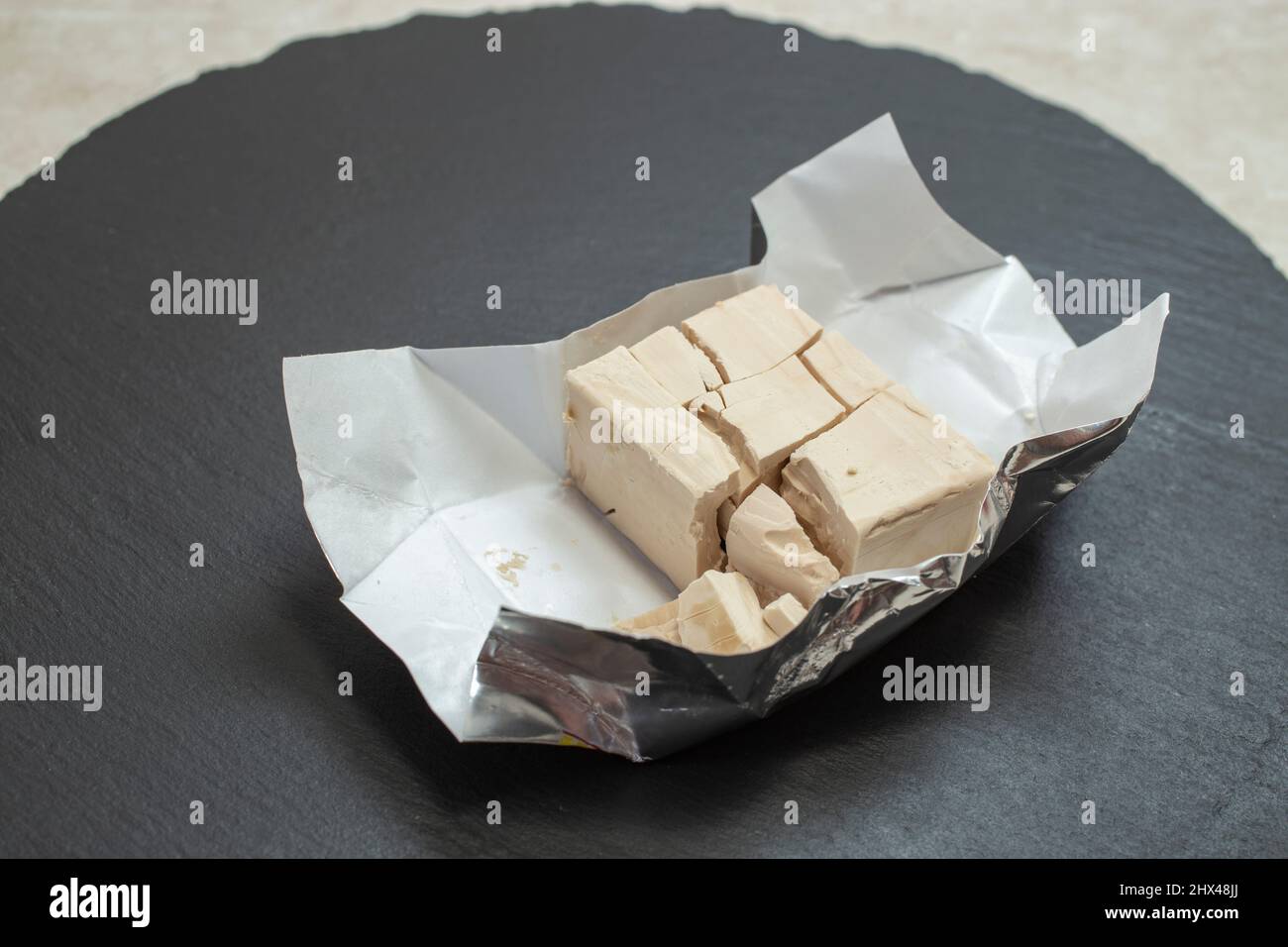 Crumbled yeast in aluminum  package on a black stone tile Stock Photo