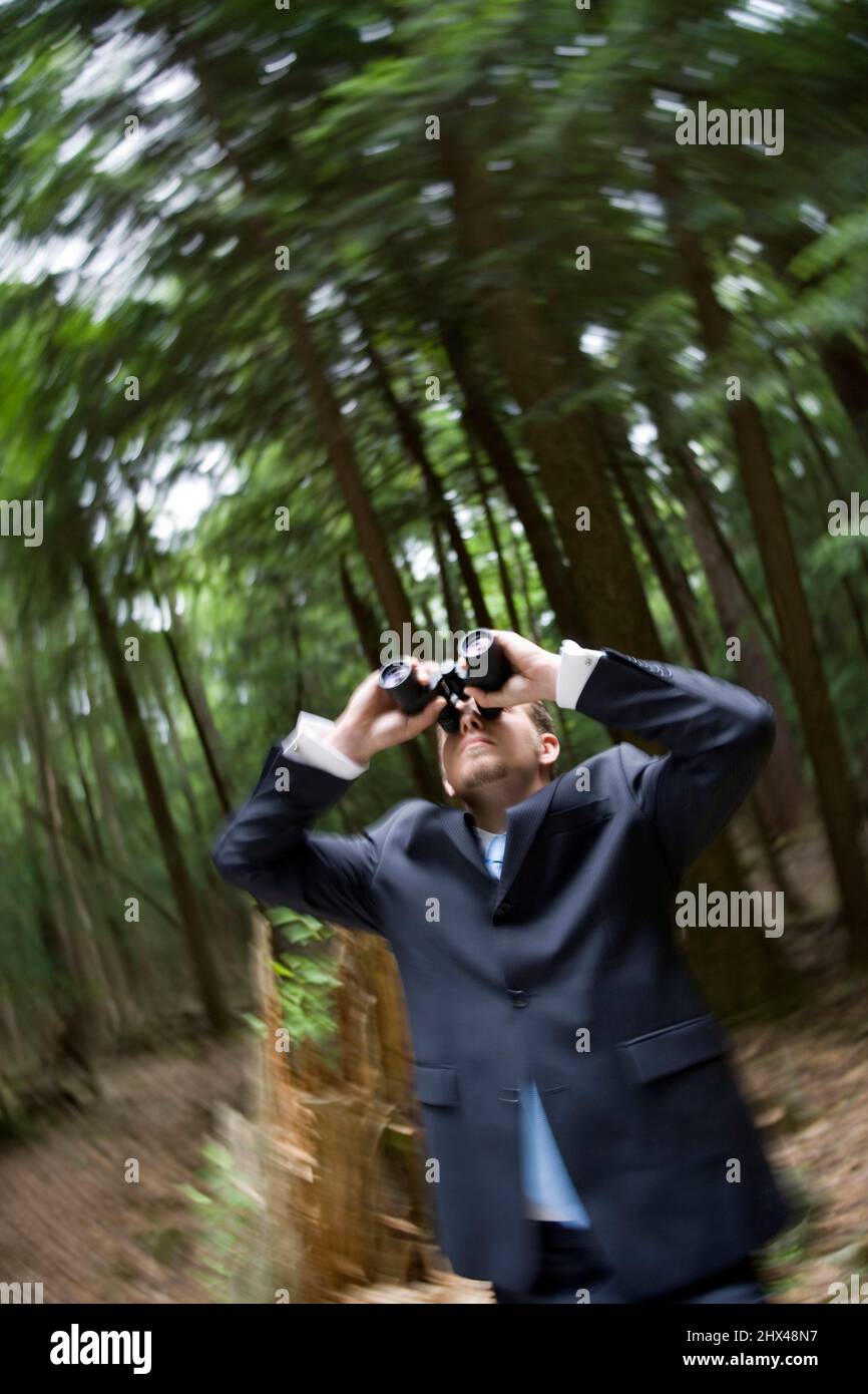 SPINNING EFFECT YOUNG BUSINESSMAN LOOKING THROUGH BINOCULARS IN TEMPERATE MIXED NORTHERN FOREST Stock Photo