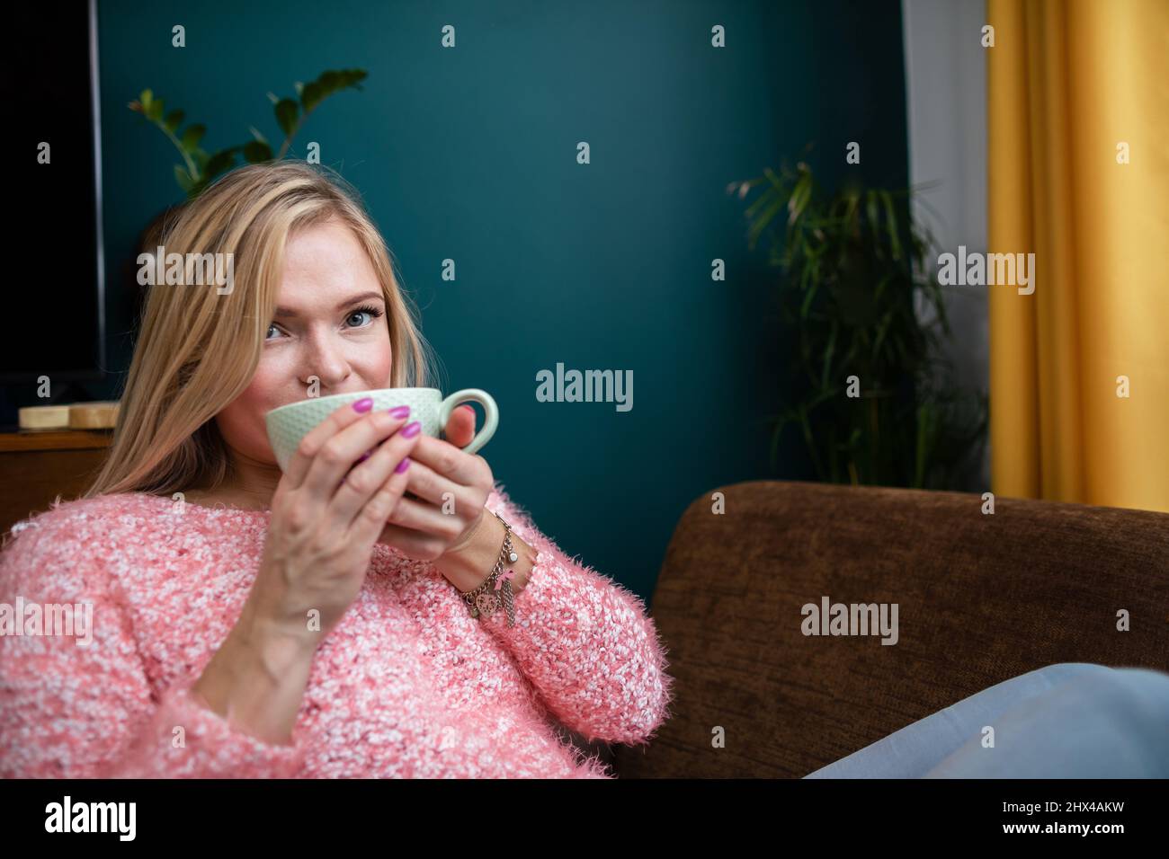 A young woman drinks coffee while sitting in the living room. Stock Photo