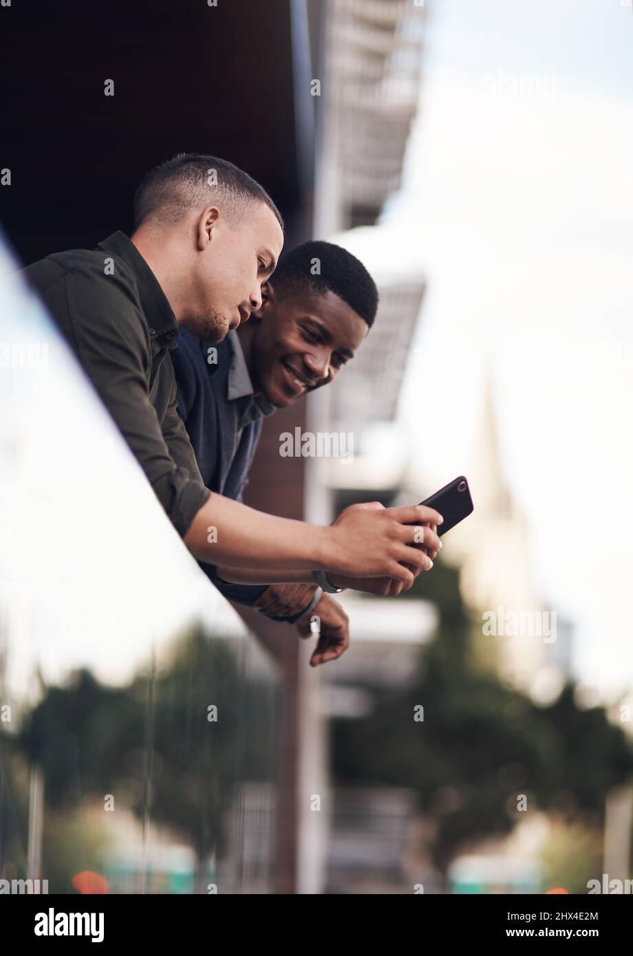 Have you seen this. Shot of two businessman looking at something on a cellphone while standing on the balcony of an office. Stock Photo