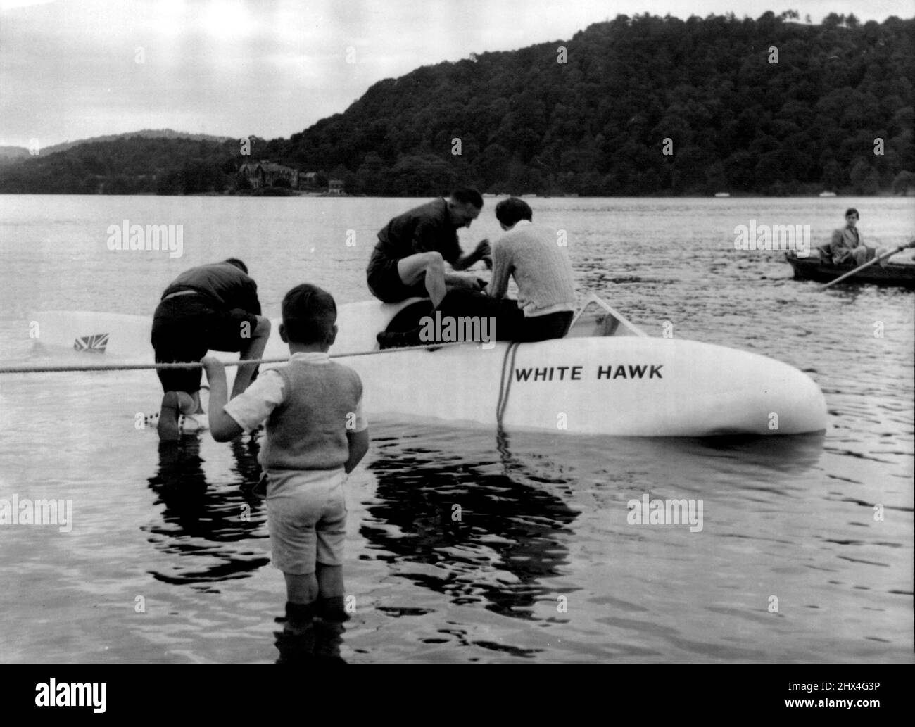 Jet-Boat Dives In Lake During Trial - The White Hawk being hauled to the shore after the mishap. Mr. Frank Hanning-Lee is seated on right.The £14,000 jet-propelled speed boat White Hawk, in which Mr. Frank Hanning-Lee, on naval officer, of Chelsea, London, and his wife Stella hope to rapture the the world's water speed record for Britain, dived briefly under the surface of the lake in a mishap during a trial run on Windermera, Mr. Hanning-Lee was piloting the boat when it was struck by side-wash from a pleasure boat. Water entered the air intake and the White Hawk dived nose first, filling wit Stock Photo