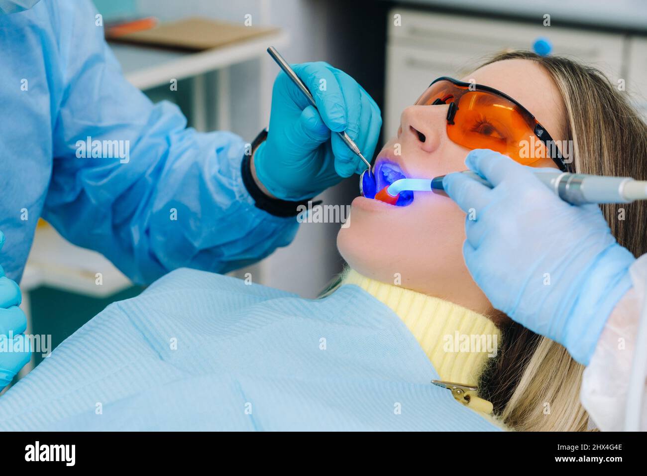 A young beautiful girl in dental glasses treats her teeth at the