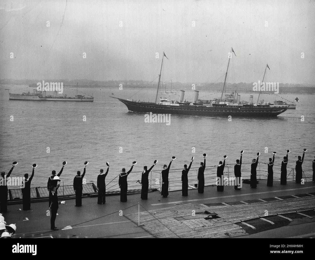 The King Reviews His Fleet At Spithead - Men of the aircraft-carrier 'Glorious' cheering as the Royal yacht 'Victoria and Albert' passed down the lines. Aboard the Royal yacht 'Victoria and Albert', the King Passed through the five-mile lines of 160 warships and merchant vessels when he made his Coronation Review of the British navy and Merchantile Marine at Spithead. Nearly 300 ships, including 17 from foreign fleets were reviewed. May 20, 1937. Stock Photo
